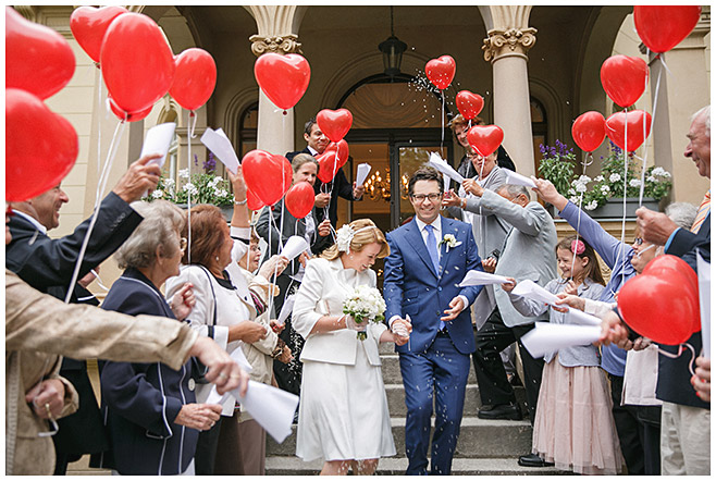 Brautpaar wird beim Auszug nach standesamtlicher Trauung in der Hochzeitsvilla des Standesamts Steglitz-Zehlendorf von Freunden mit roten Herzluftballons empfangen © Hochzeitsfotograf Berlin hochzeitslicht