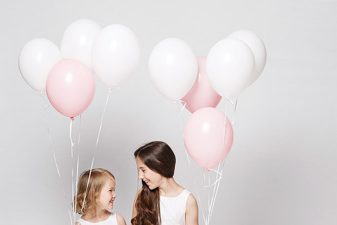 Kinderfoto von zwei Schwestern mit weißen und rosa Luftballons aufgenommen bei Kinderfotoshooting mit professionellem Kinderfotograf Berlin © Fotostudio Berlin LUMENTIS